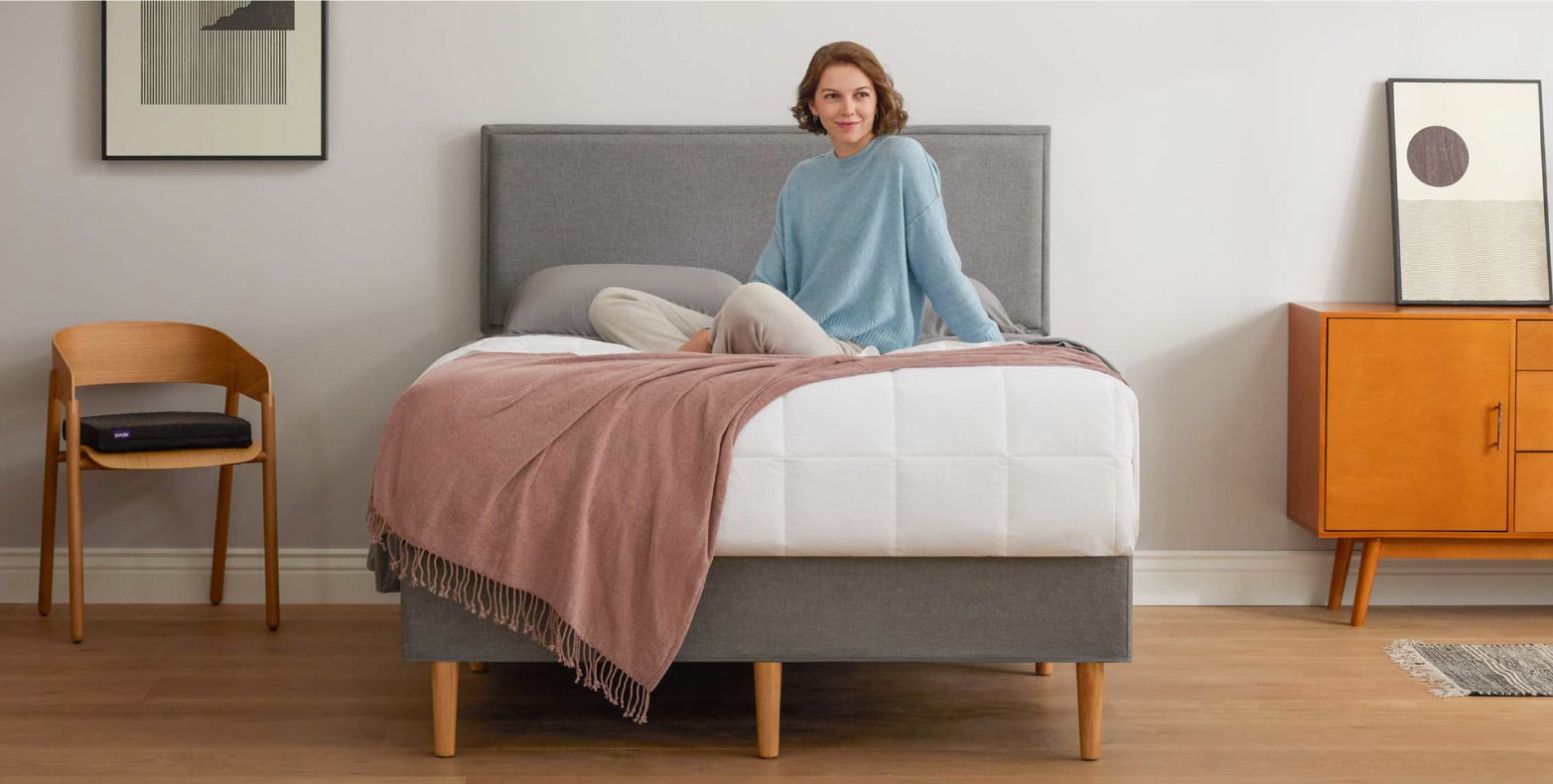 A young woman sits on the bed with a wooden mattress foundation.