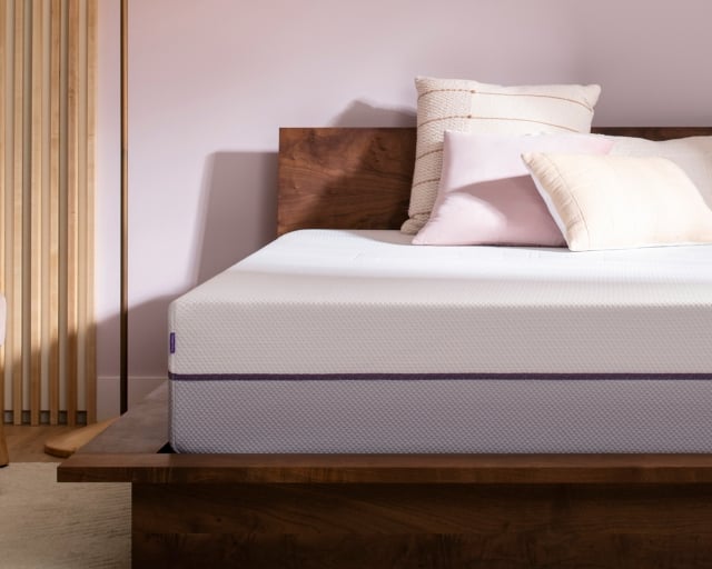 An unmade Purple Plus mattress with decorative pillows in a modern bedroom.