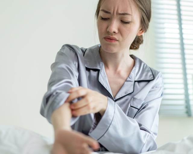 A person itching their arm while sitting in bed.