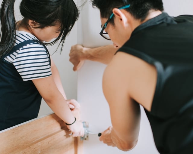 An adult and a child adjust the joints on a squeaky bed frame.