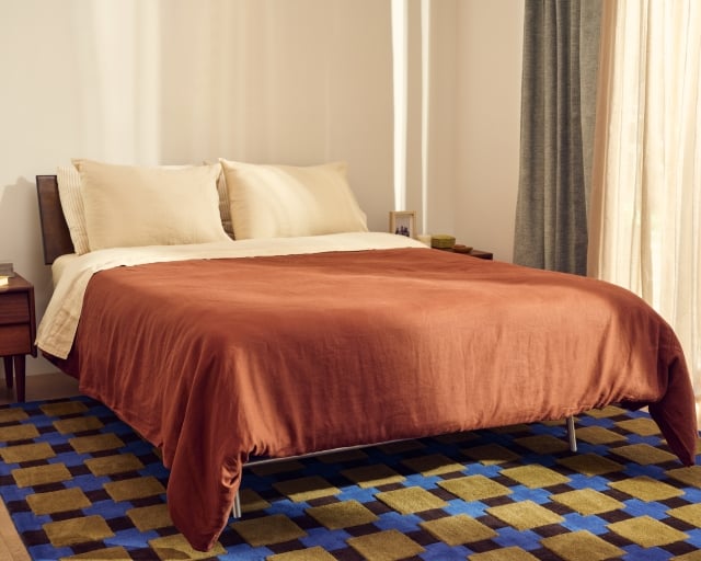 A Purple mattress with a dark orange duvet.