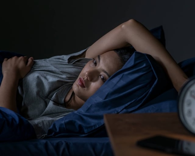 A young woman struggling with insomnia lies awake at night.
