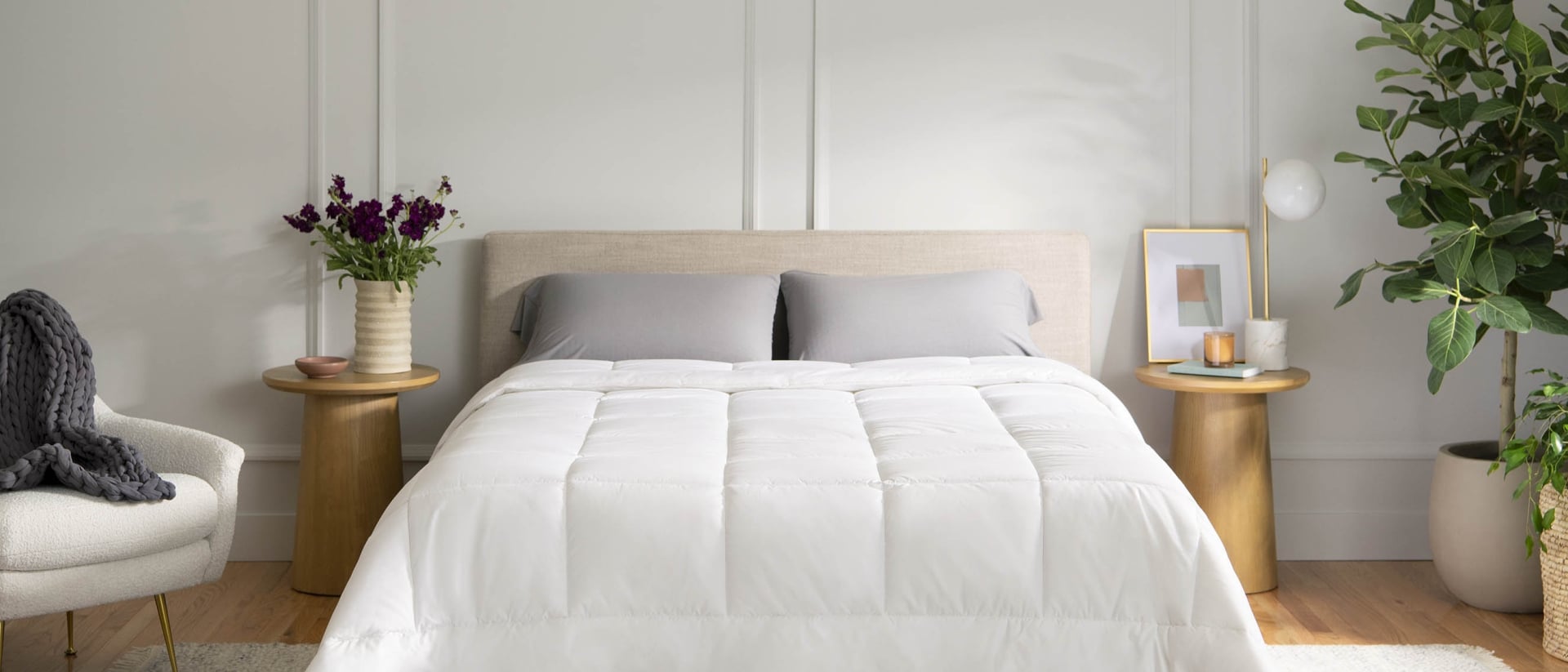 A queen bed with white and grey bedding between two wooden nightstands.