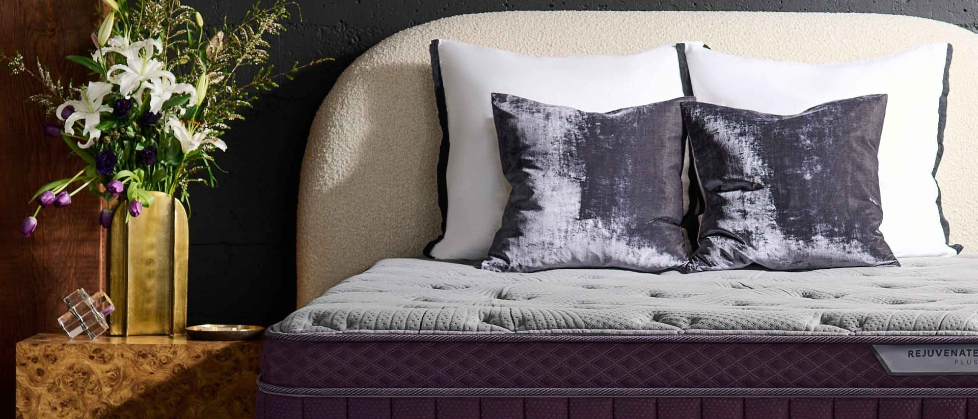 Purple RejuvenatePlus™ Mattress on a sherpa bed frame next to a nightstand with a large bouquet.