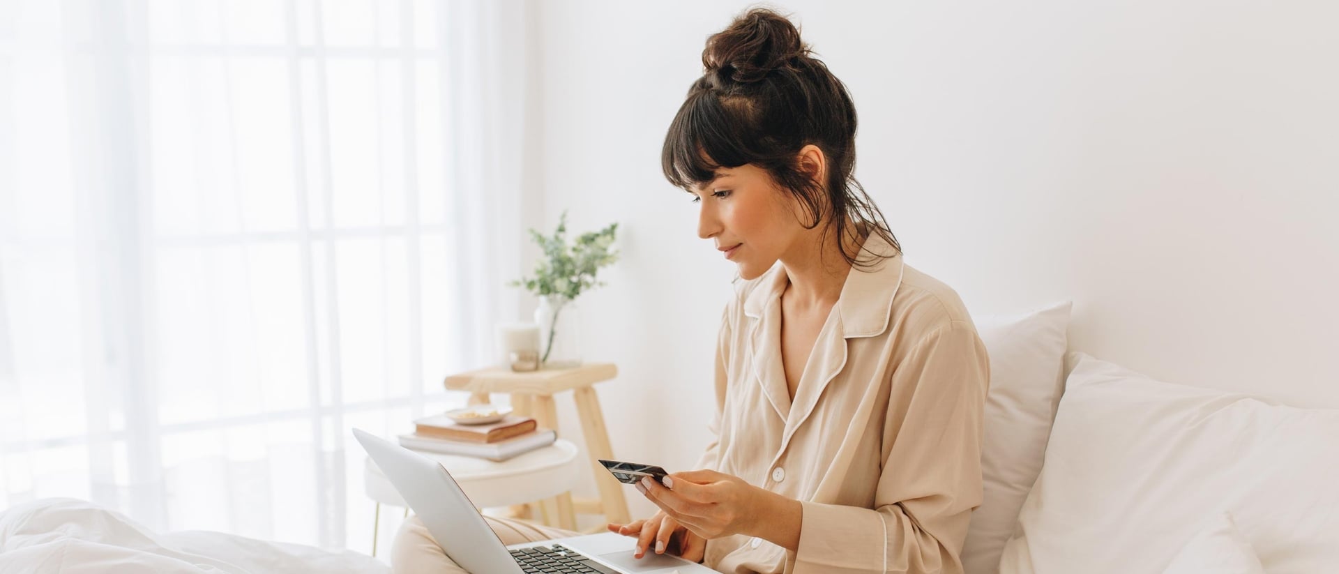 A woman in bed using a laptop to buy a mattress online.
