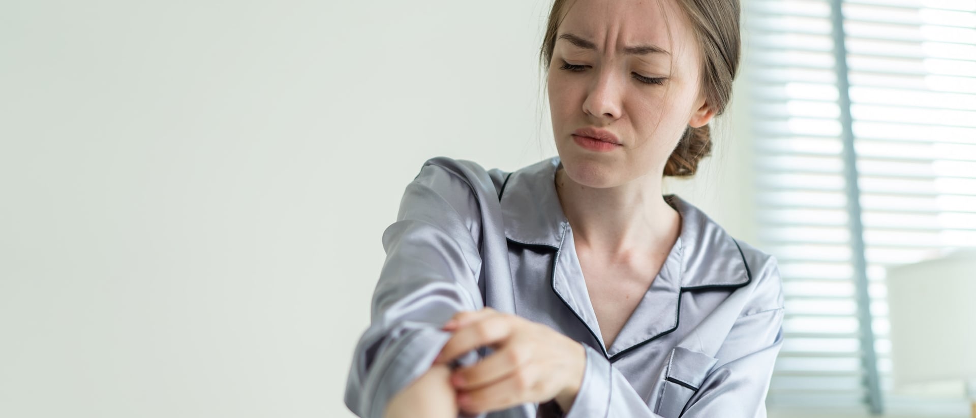 A person itching their arm while sitting in bed.